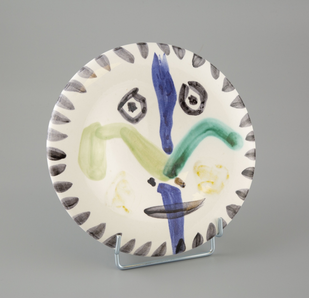 63- Pabli Picasso-Madoura. Visage n°144. Assiette en terre de faience à décor aux engobes noir, vert, bleu, jaune. D.25cm. Adjugé 6200€